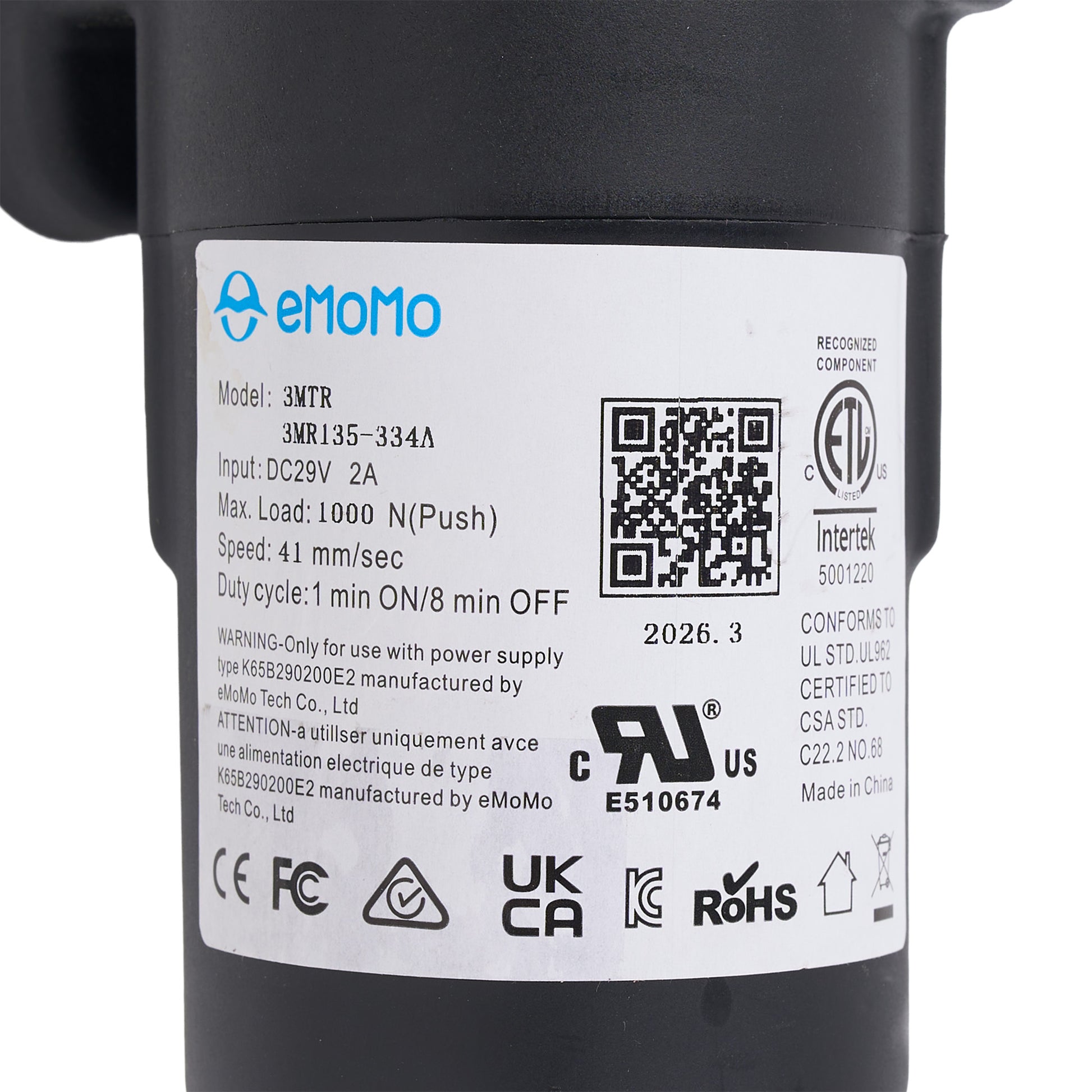 Close-up of a black cylindrical product with a white label showing the eMoMo brand, model 3MTR, and various certification logos including UL, CE, and RoHS.