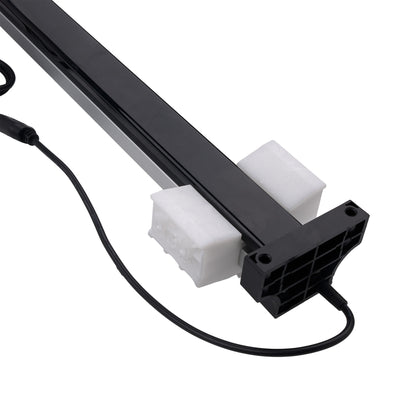 A close-up of a black linear light fixture or LED strip with a black power cable, resting on two white foam blocks against a plain white background.