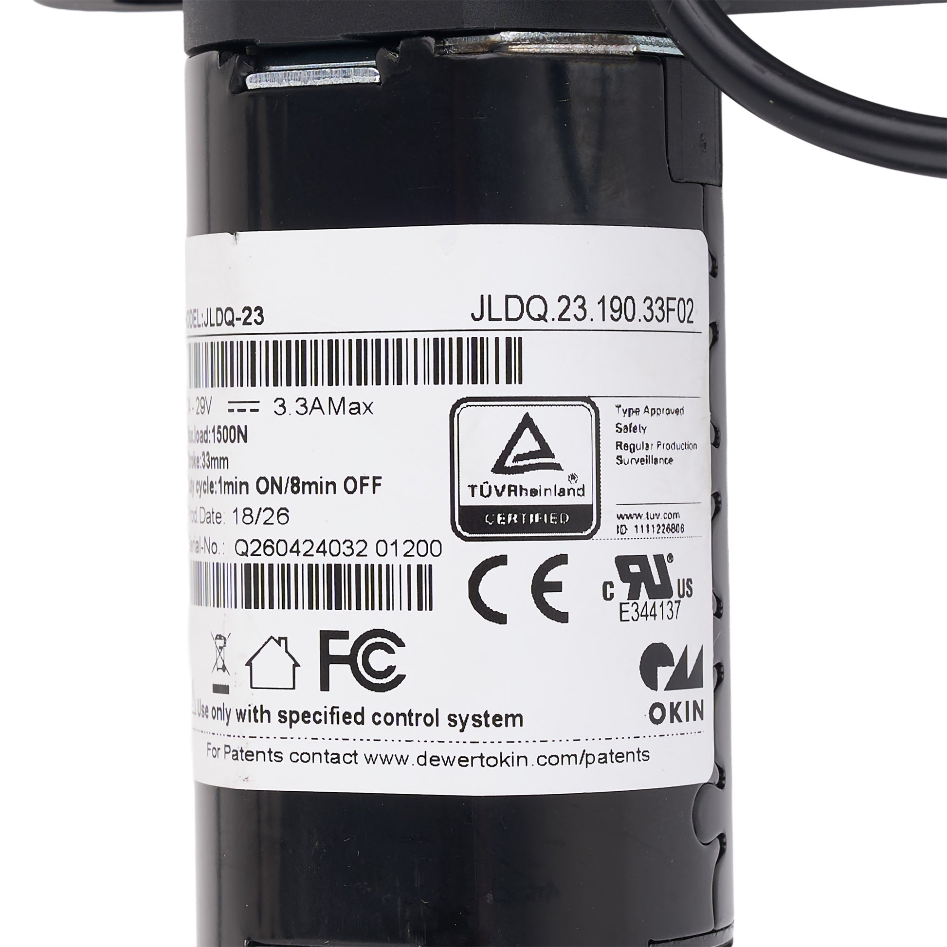 Close-up of a black cylindrical industrial component with a large white label showing barcodes, certification marks including TÜV Rheinland and FCC, and printed text including JLDQ.23.
