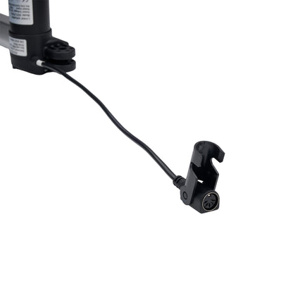 A close-up of a black mechanical component with a short black cable leading to a black clamp-like connector, shown on a plain white background.