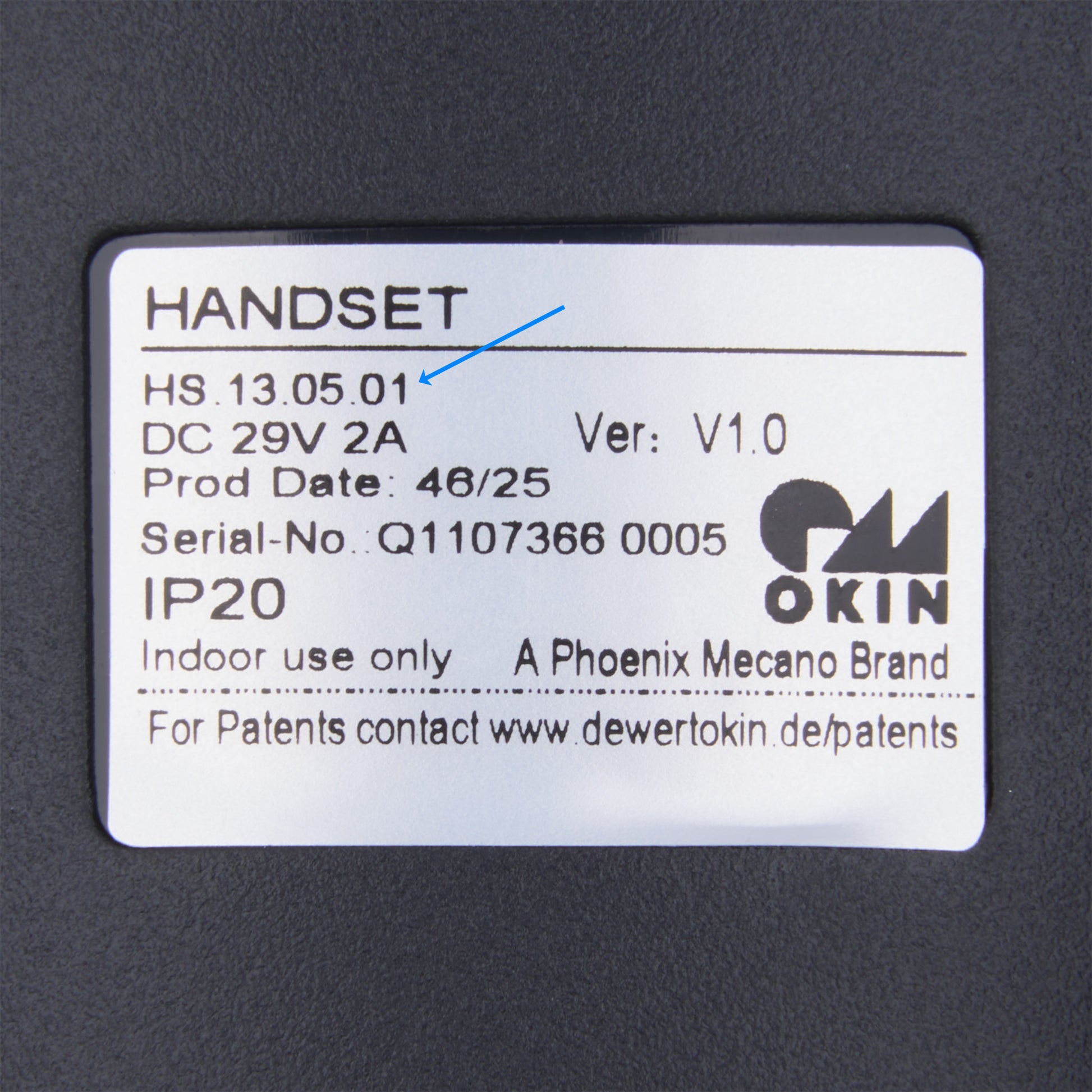 A close-up of a white product label on a dark gray surface, showing text including 'HANDSET', 'OKIN', 'Phoenix Mecano Brand', and 'A PHOENIX MECANO BRAND'.